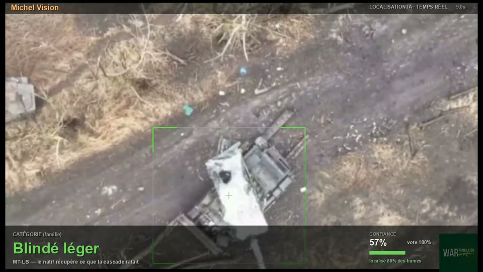 Véhicule chenillé peint en blanc, vu du ciel sur une piste de terre, encadré en vert.